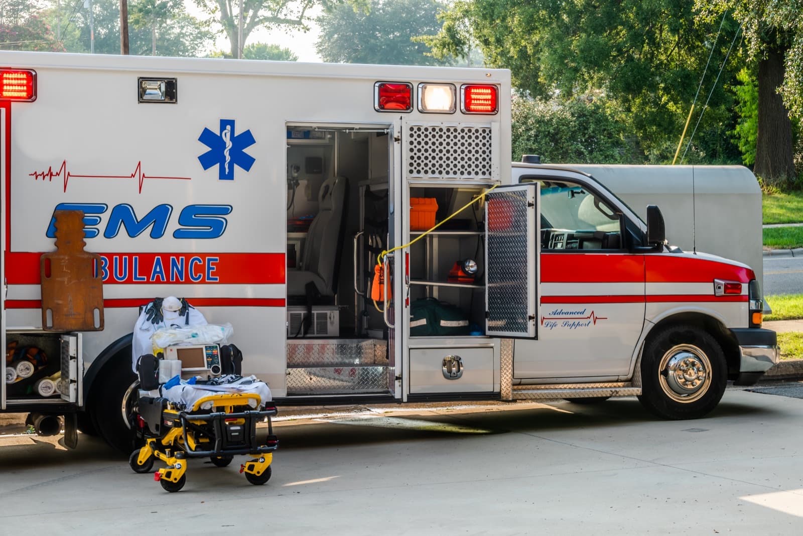 An ambulance parked with its rear doors open, stretcher and equipment staged alongside.